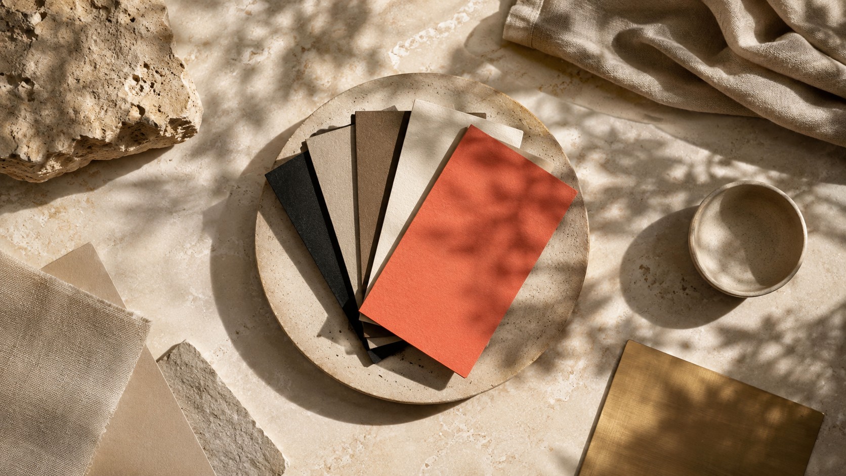 Nuancier papier posé à plat mêlant beige, taupe, noir et pierre, avec un seul accent corail