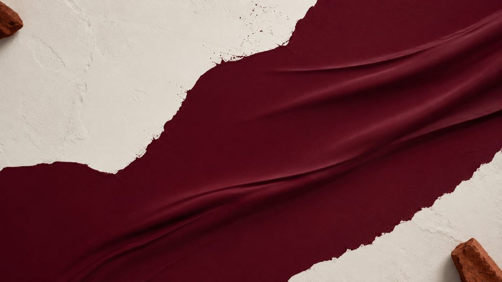 Matière bordeaux mate étendue sur une surface beige texturée, évoquant un rouge assombri pour une marque premium